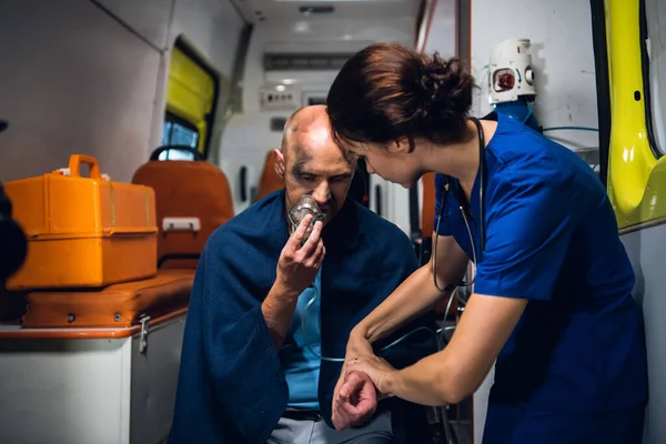 Женщина-парамедик проверяет пульс своих пациентов и задаёт ему вопросы. — стоковое фото