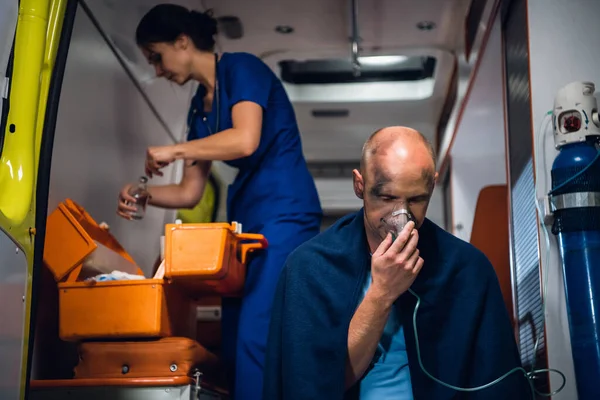 Медицинский работник, готовящий трубку, человек в кислородной маске на переднем плане — стоковое фото