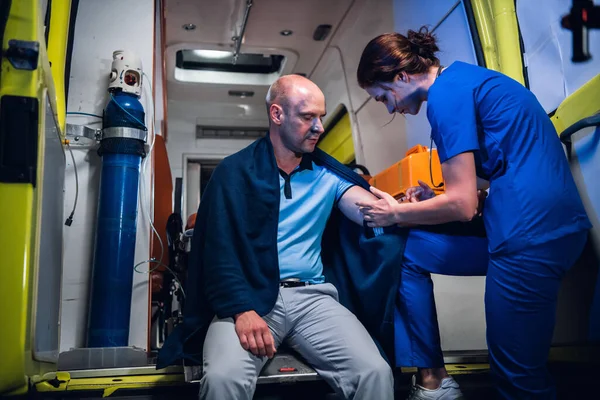 Üniformalı genç bir hemşire ambulans arabasında hastasına iğne yapıyor.