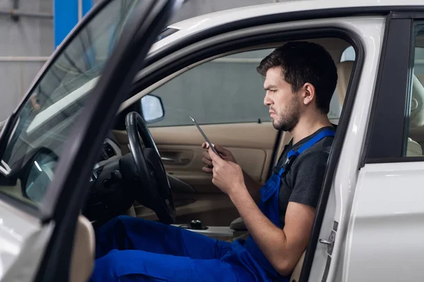 Araba servisi çalışanı arabada oturuyor ve telefon kullanıyor.