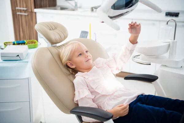Una niña rubia sentada en el consultorio de dentistas — Foto de Stock