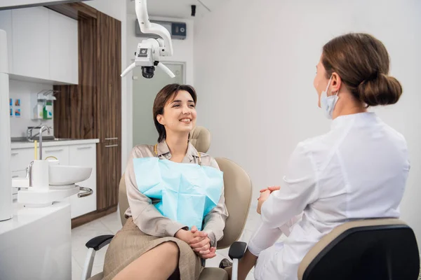 People, medical, stomatology and health care concept - A woman at the dentists office chatting to her doctor and smiling with a toothy smile — Foto de Stock