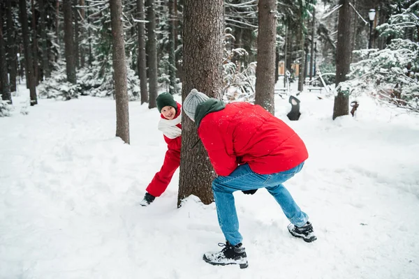 Мужчина в красной куртке в зимнем лесу, играет в догонялки со своим племянником, мальчик в красном зимнем комбинезоне и шарфе — стоковое фото