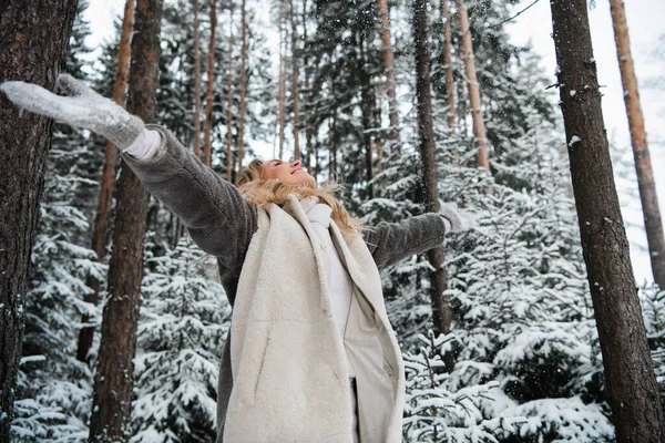 Счастливая молодая женщина наслаждается снегопадом зимой за пределами города в лесу — стоковое фото