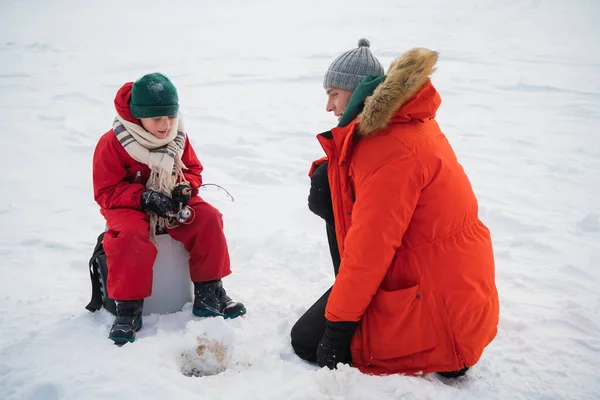 Padre e hijo en ropa roja de invierno vinieron a pescar en la orilla del río en invierno —  Fotos de Stock