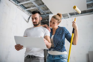 A woman hugs a man from behind, he looks at the scheme of the apartment