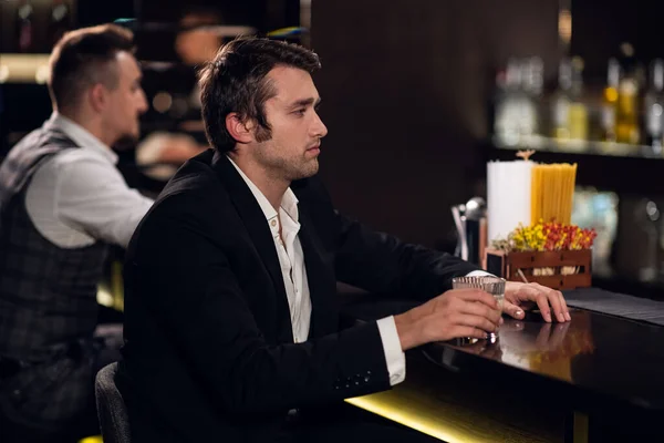 Молодий чоловік п'є коктейль у барі, спілкується з барменом — стокове фото
