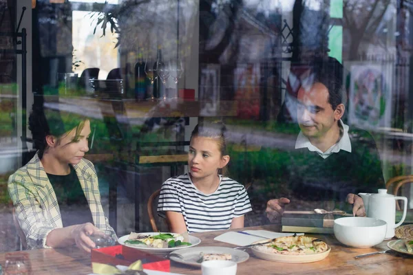 Une fille déjeunant avec ses parents, vue par la fenêtre — Photo