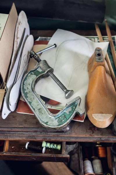 Inside the drawer of the wooden table are threads and needles, on the table paper drawings, blanks, insoles, tools — Foto de Stock