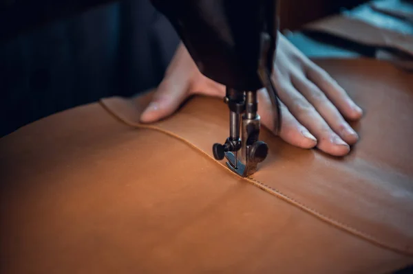 El primer plano de la guía de la aguja de la máquina de coser hace una costura uniforme con un hilo en un paño marrón de cuero genuino. Las manos del zapatero — Foto de Stock