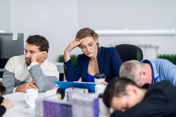 Business people sleeping in the conference room during a meeting, while their colleague is trying to concentrate on the documents she is studying