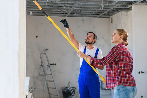 Un trabajador le dice a una mujer cómo pintar una pared correctamente — Foto de Stock