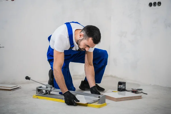 Trabajador en ropa de trabajo azul utiliza un cortador de azulejos — Foto de Stock