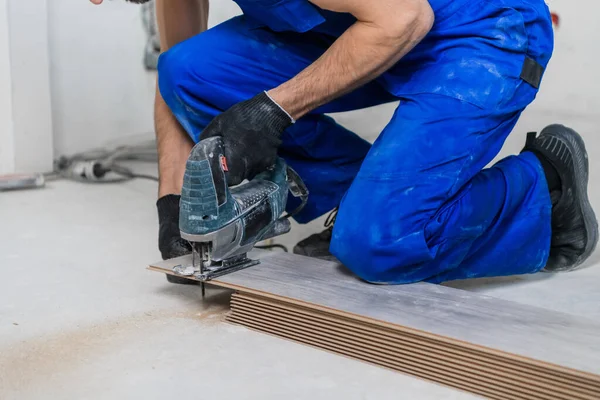 Een voorman in een overall snijdt planken en legt laminaatvloeren — Stockfoto