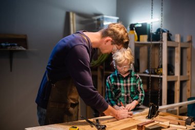 Genç bir baba, garajda oğluna marangozluğu öğretiyor..