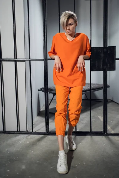 Молодий злочинець спирається на ґрати клітини в помаранчевому халаті. Жіноча в'язниця максимальної безпеки . — стокове фото