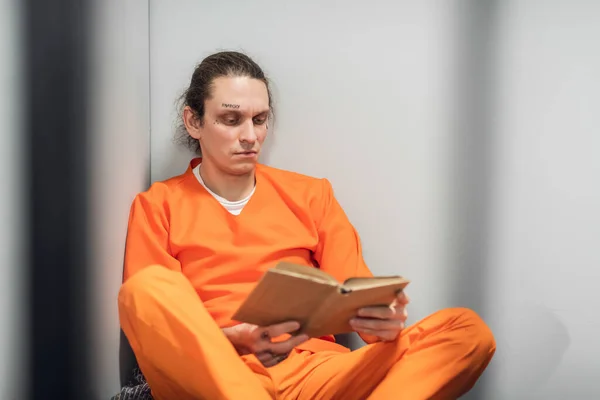 Молодого в'язня з татуйованим обличчям віддалено тренують у камері. Читає підручник, що сидить на бункері . — стокове фото