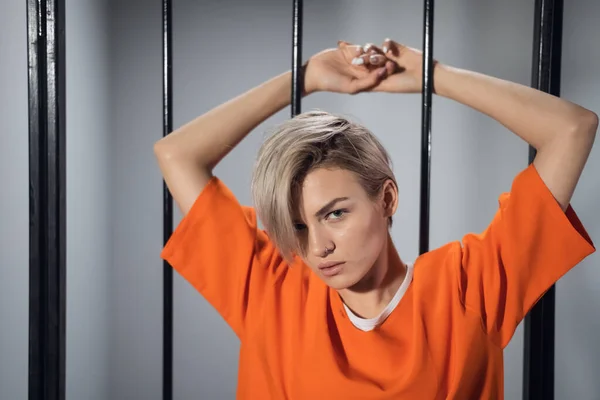 A close-up portrait of an orange-robed prisoner in prison against the background of prison bars — Stock Photo, Image