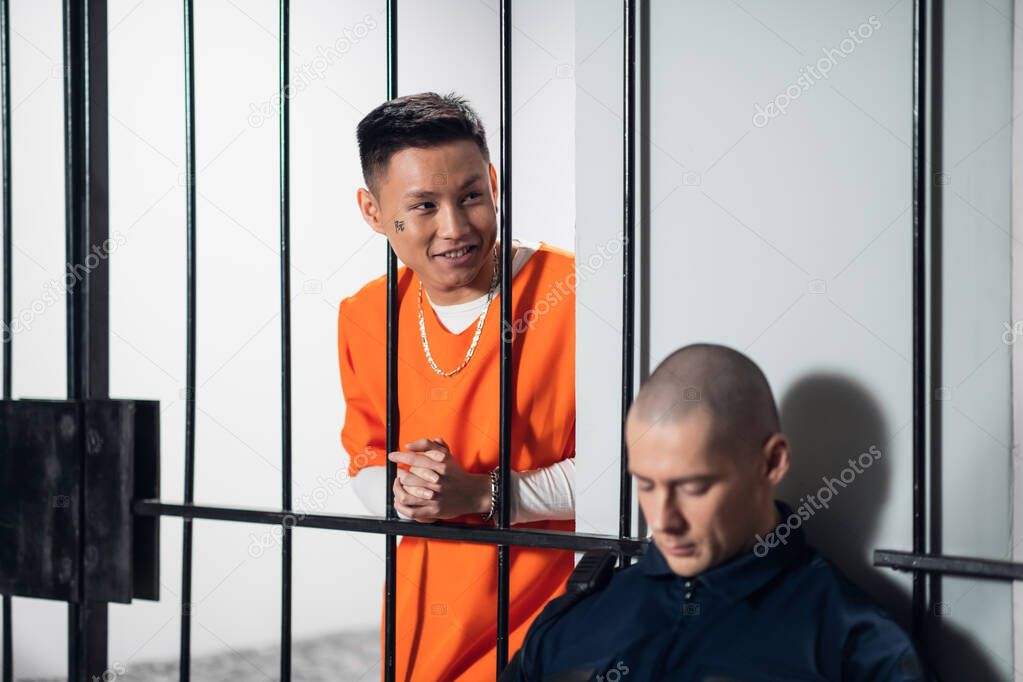 White and asian dangerous criminals and serial killers attack the armed guard who guards their cells. Stretching out his hands to the security guard through the bars.