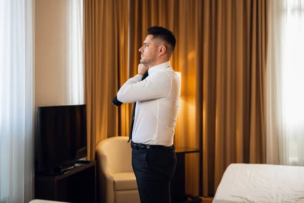 A young man dressing up in a hotel room, side view