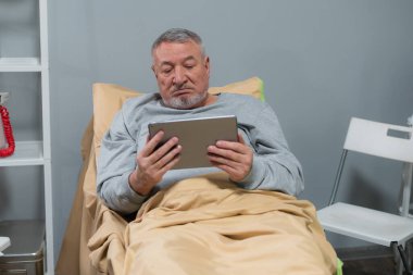 Bakımevinde hesabına e-kitap okuyan gri saçlı bir adam.