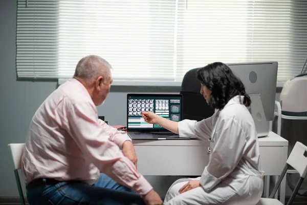 Médica com um velho a olhar para o raio-X, a médica está a explicar o que vê lá dentro. — Fotografia de Stock