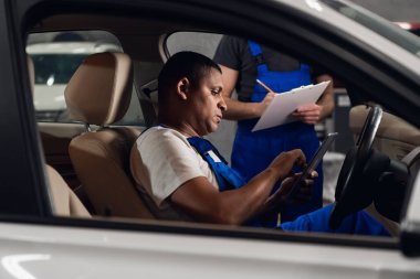 Bir atölye çalışanı arabada tablet kullanıyor.