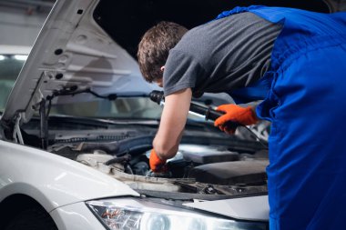 Bir tamirci, araba motorunu lamba kullanarak kontrol eder.