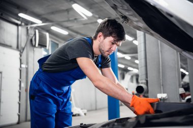 İşçi arabanın kaputunun altındaki motoru kontrol ediyor.