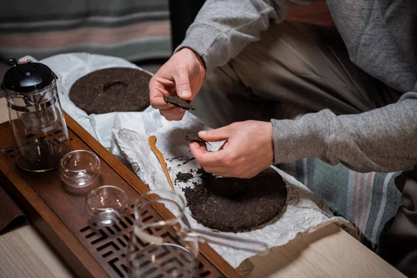 Der Vorbereitungsprozess für die Teezeremonie ist ein wichtiger. Männerhände brechen den Tee zum Aufbrühen in einer Keramik-Teekanne, um ihre Nasen zu behandeln. — Stockfoto