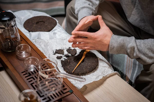 Set für eine Teezeremonie in Nahaufnahme. Ein Mann mit einer Teenadel zerbricht einen Teekuchen aus starkem alten reifen Tee, um das Aroma zu genießen. — Stockfoto