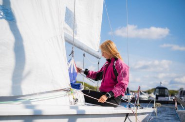 Pembe ceketli genç bir sporcu nehirde tek direkli bir yatı donatmak için antrenman yapıyor..