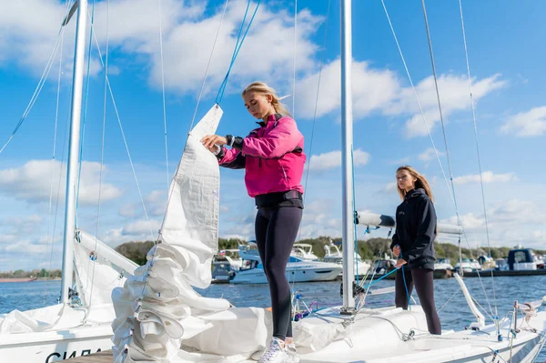 Two young female athletes prepare a sailing boat for the regatta on the river pier — Stock Photo, Image