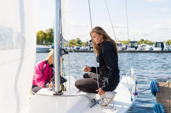 Before a trip on the river, young cute girls equip their one-masted yacht, prepare for the trip