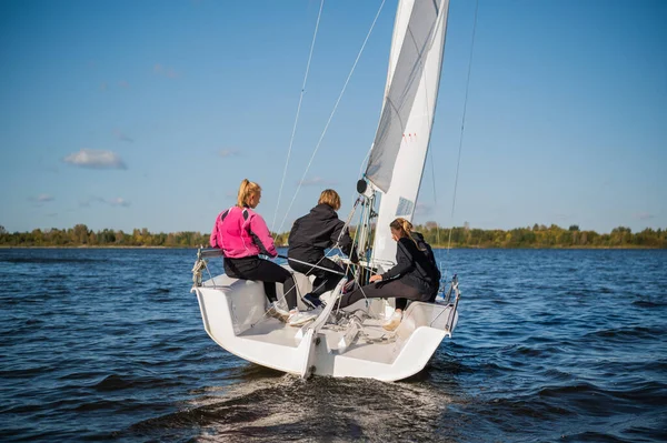 A beautiful white yacht is sailing in the wind on the river against the background of a beautiful autumn forest. A guy on board with two girls.