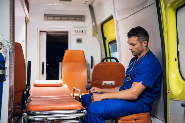 Уставший мужчина в медицинской форме сидит в машине скорой помощи — стоковое фото