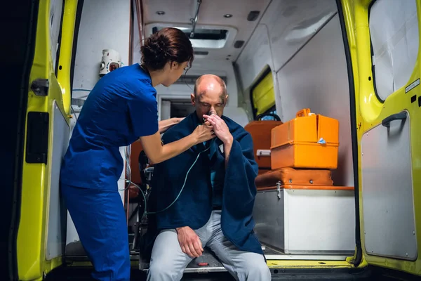 Una joven enfermera con uniforme le da una máscara de oxígeno a un hombre herido en una manta —  Fotos de Stock