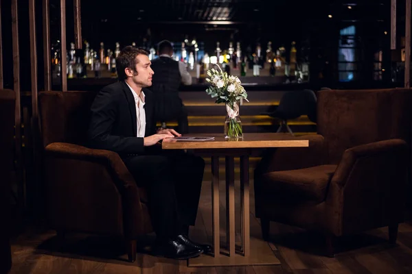 a single man in a jacket sits at a table in a restaurant after work