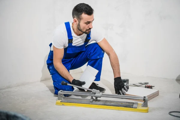 Een man in een blauwe overall snijdt een tegel met een snijplotter — Stockfoto