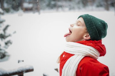 Kırmızı, kalın bir ceket ve örgü bir şapka giymiş yaramaz bir çocuk düşen kar tanelerini diliyle yakalar..
