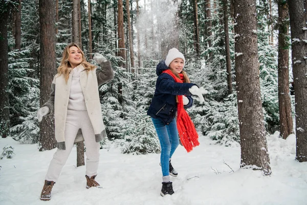 Милая молодая мама и ее дочь-подросток вышли на прогулку зимой, чтобы поиграть в снежки друг с другом — стоковое фото