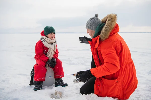 Um pai pescador experiente ensina seu filho a lidar com artes para a pesca de inverno, eles fizeram um buraco e peixe nele. — Fotografia de Stock