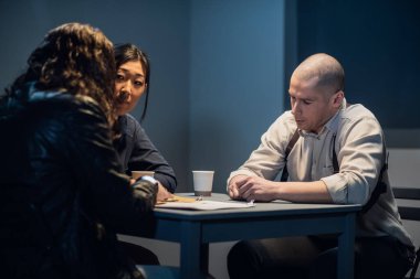 Sorgu odasında, müfettiş ve memur suçluyla konuşuyor.