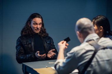 Genç polisler sorguluyor, şüpheli cesurca gülüyor.