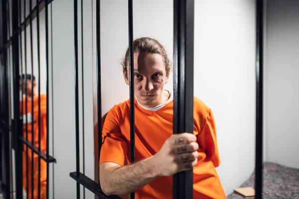 Retrato psicológico de un prisionero malvado y salvaje a través de los barrotes de una celda de prisión. Una mirada fuerte y emociones. — Foto de Stock