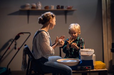 Güzel bir kız ve sarışın bir çocuk bir sanat stüdyosunda çömlekçi çarkında bir tabak yontuyorlar..