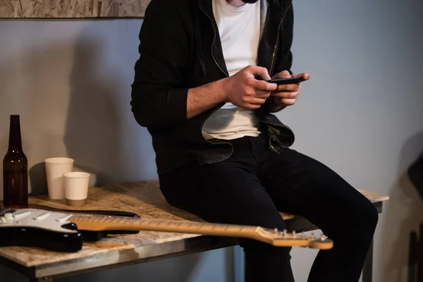 in a music Studio a guy sits on a table and plays a video game on his phone after a rehearsal.