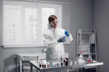 A scientist in protective eyewear and white overalls standing at the table in the science laboratory, working on something