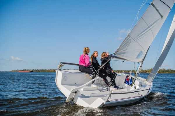 A beautiful white yacht is sailing in the wind on the river against the background of a beautiful autumn forest. A guy on board with two girls.