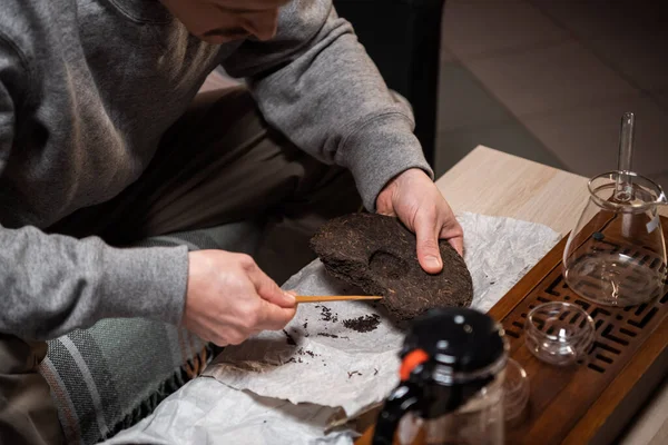 Set für eine Teezeremonie in Nahaufnahme. Ein Mann mit einer Teenadel zerbricht einen Teekuchen aus starkem alten reifen Tee, um das Aroma zu genießen. — Stockfoto